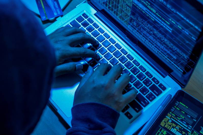 A blue-tinted image of hands typing on a laptop keyboard.